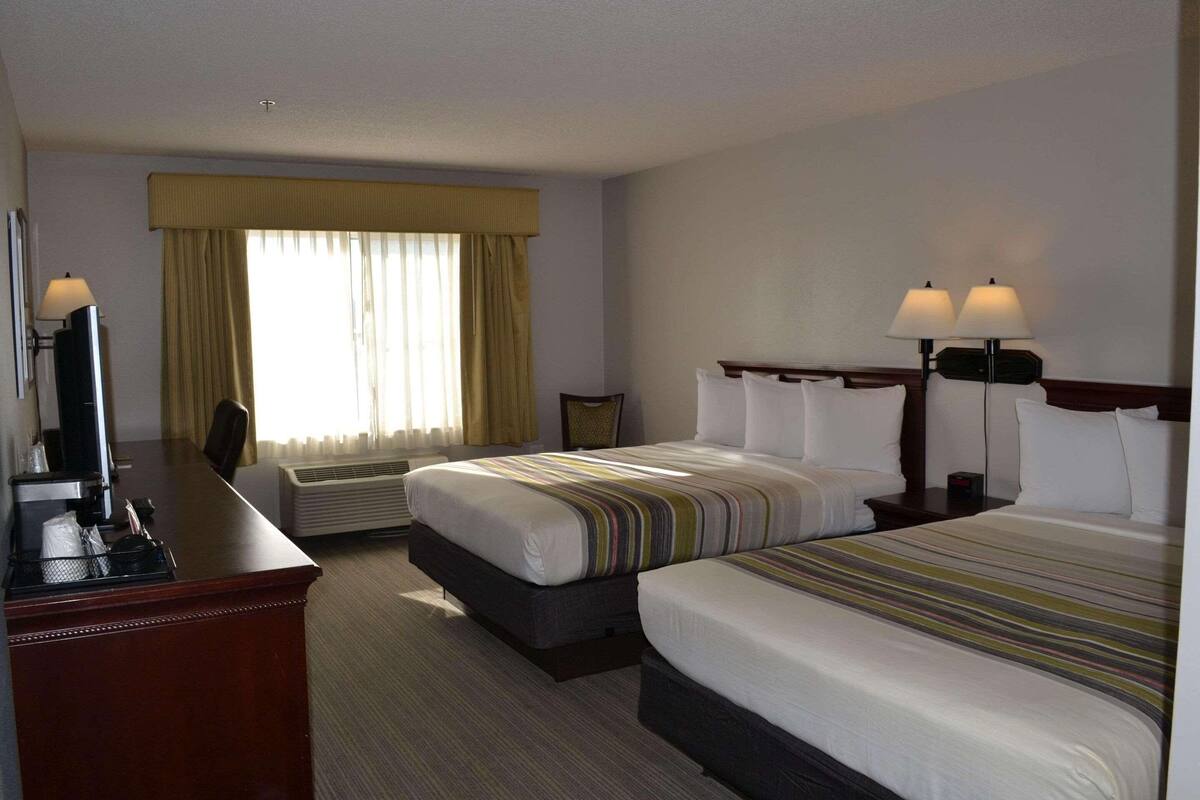 A hotel room with two beds, a desk with a computer, and a window with curtains.