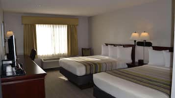 A hotel room with two beds, a desk with a computer, and a window with curtains.