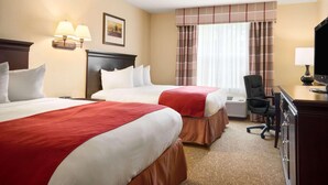 A hotel room with two beds, a desk, a chair, a television, and a window with curtains.