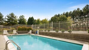 A swimming pool with a white fence, lounge chairs, and a stone wall.
