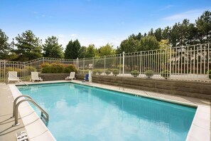 A swimming pool with a white fence, lounge chairs, and a clear sky.
