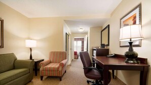 A hotel room with a green sofa, a striped armchair, a desk with a lamp, and a mirror on the wall.