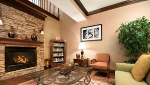 A living room with a stone fireplace, a bookshelf, a glass coffee table, a green sofa, and a large plant.