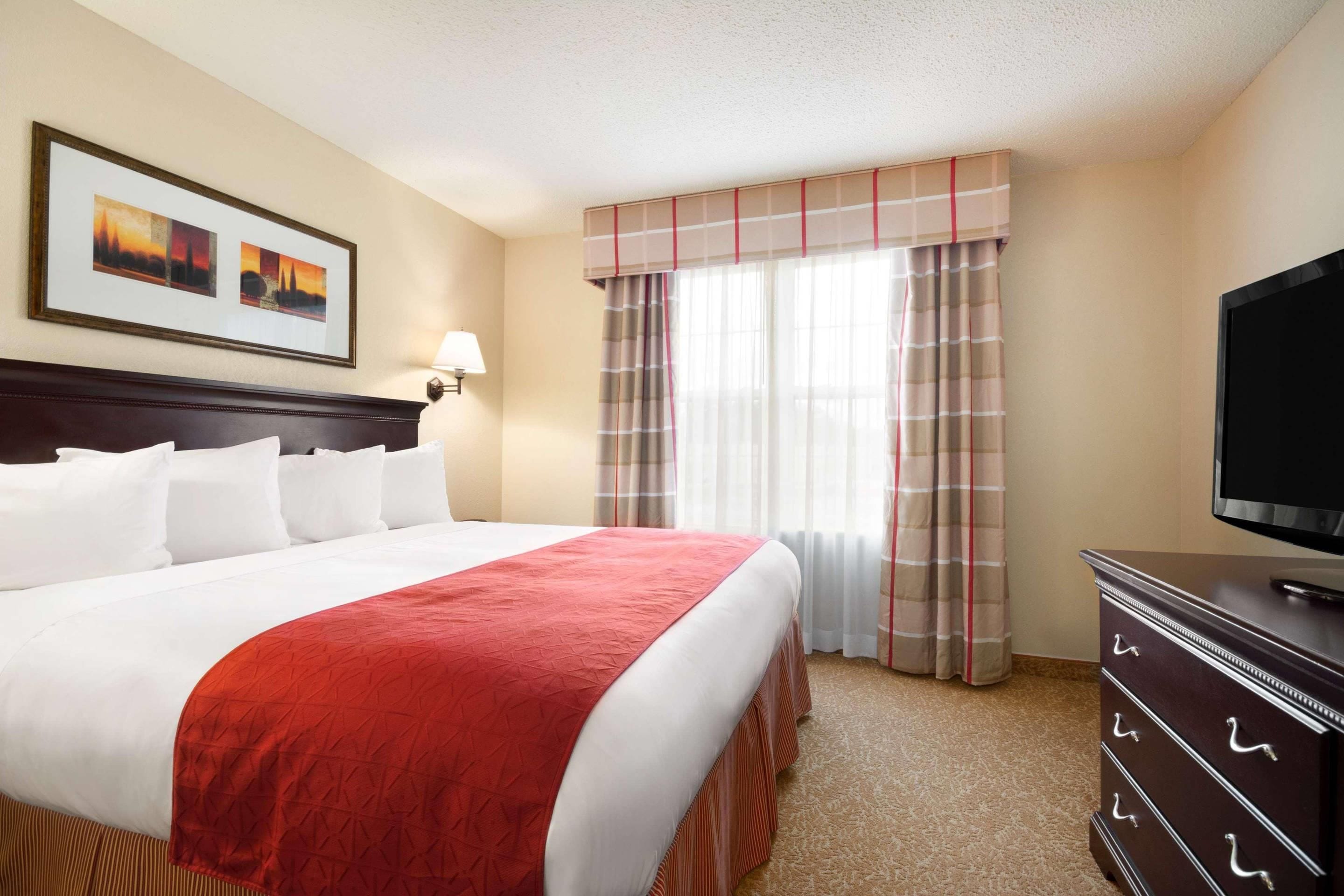 A hotel room with a large bed, a television, a dresser, and a window with curtains.