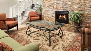 A living room with a glass coffee table, a fireplace, a staircase, and a large rug. - Country Inn & Suites by Radisson, Columbus West, OH (Columbus)