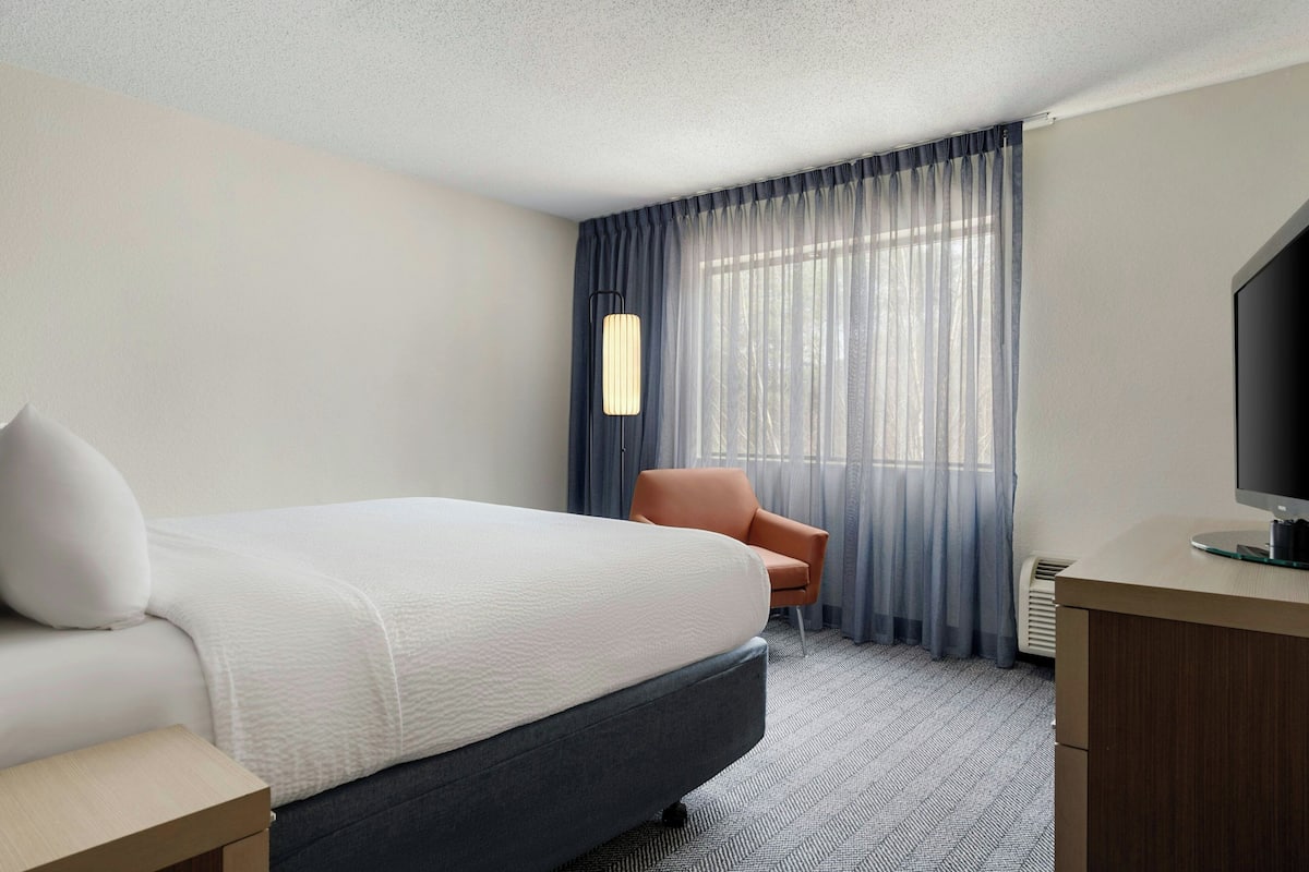 A hotel room with a bed, a desk, a chair, a television, and a window with curtains.