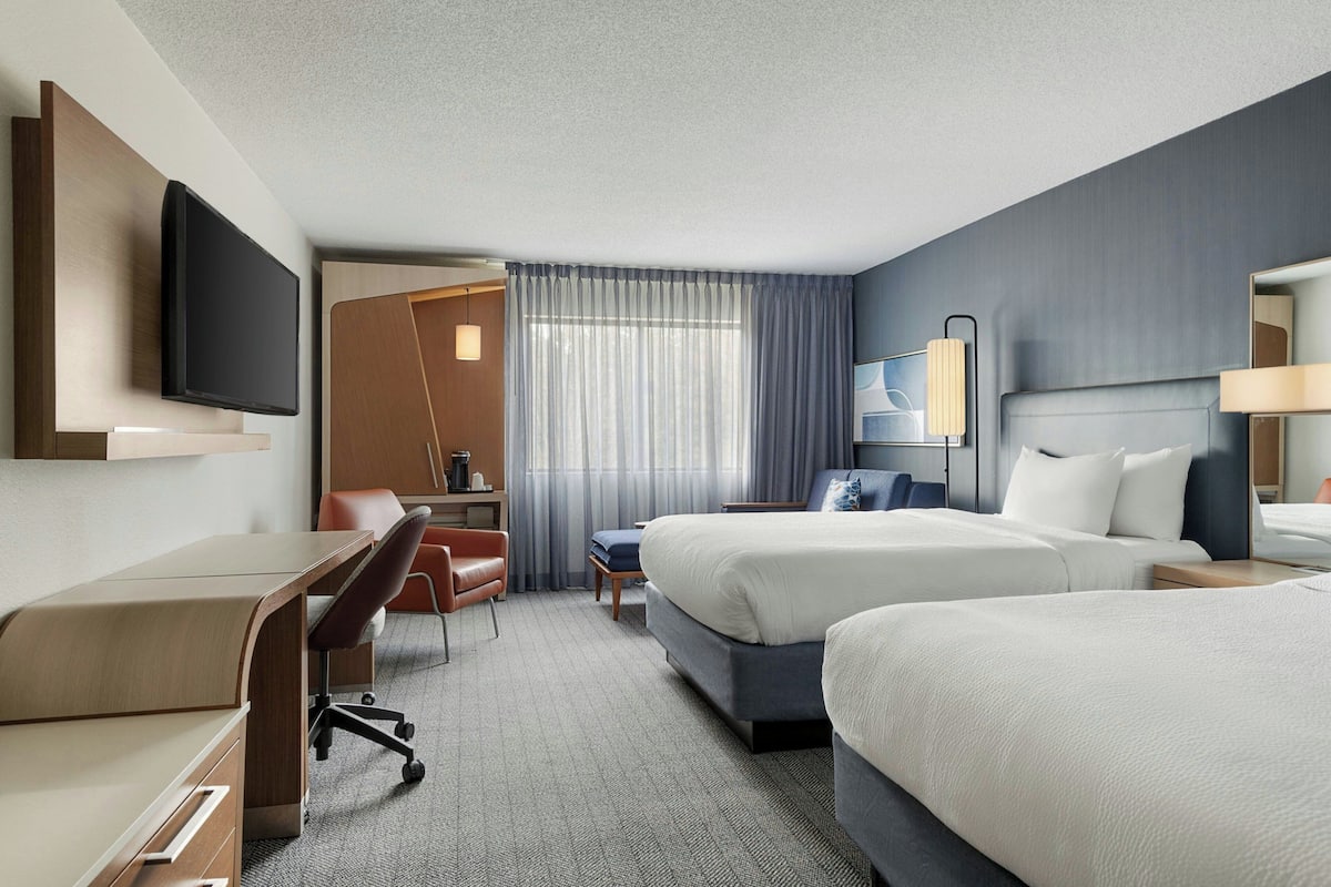 A hotel room with a desk, two beds, a TV, and a window with curtains.