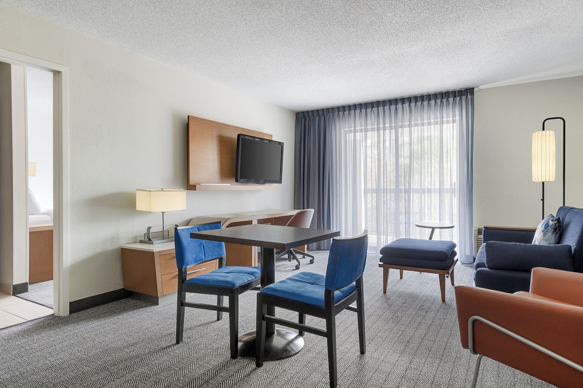 Habitación de hotel con una mesa de comedor, sillas, un televisor montado en la pared, un sofá y una lámpara.