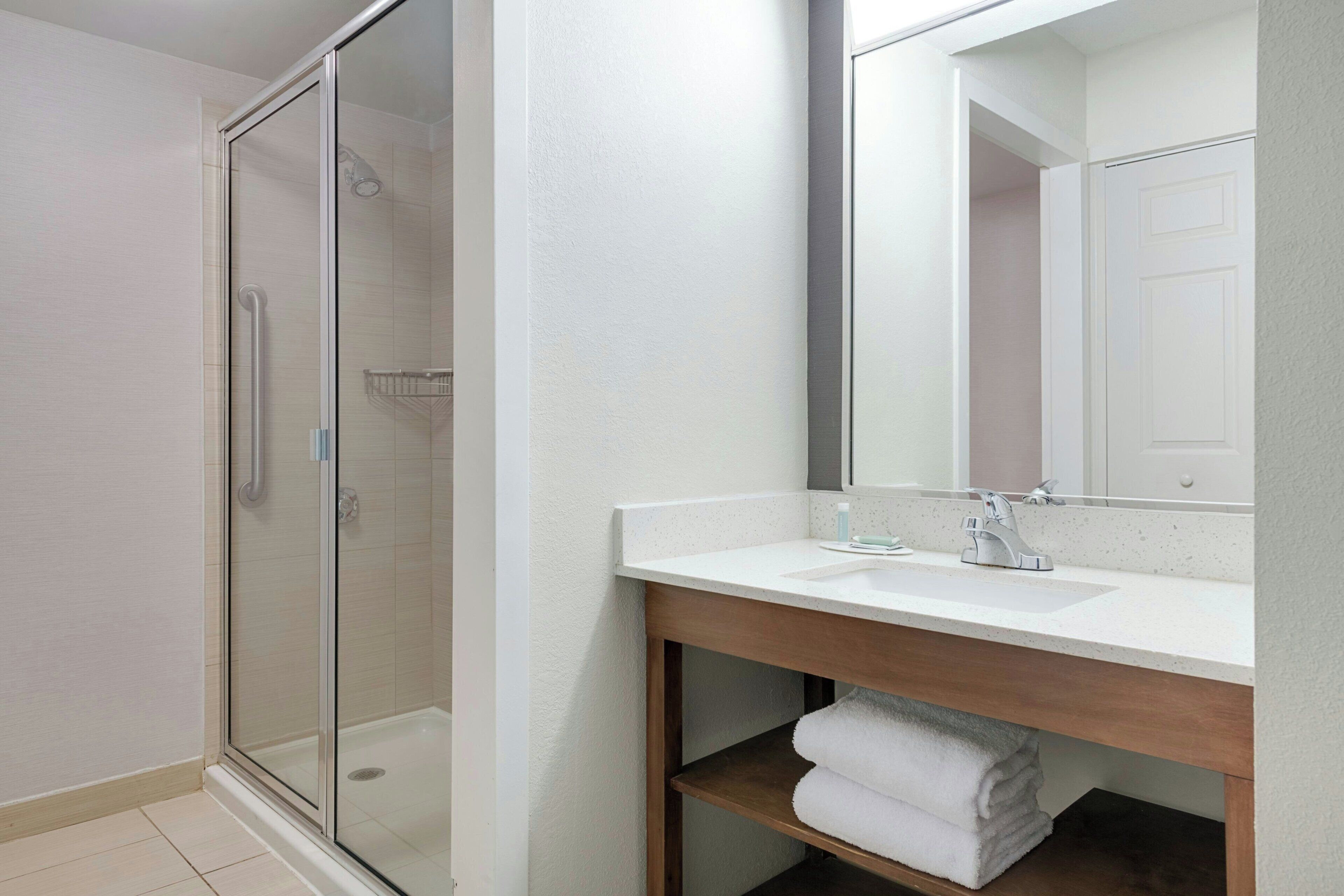 A modern bathroom with a glass-enclosed shower, a white sink, and a wooden vanity.
