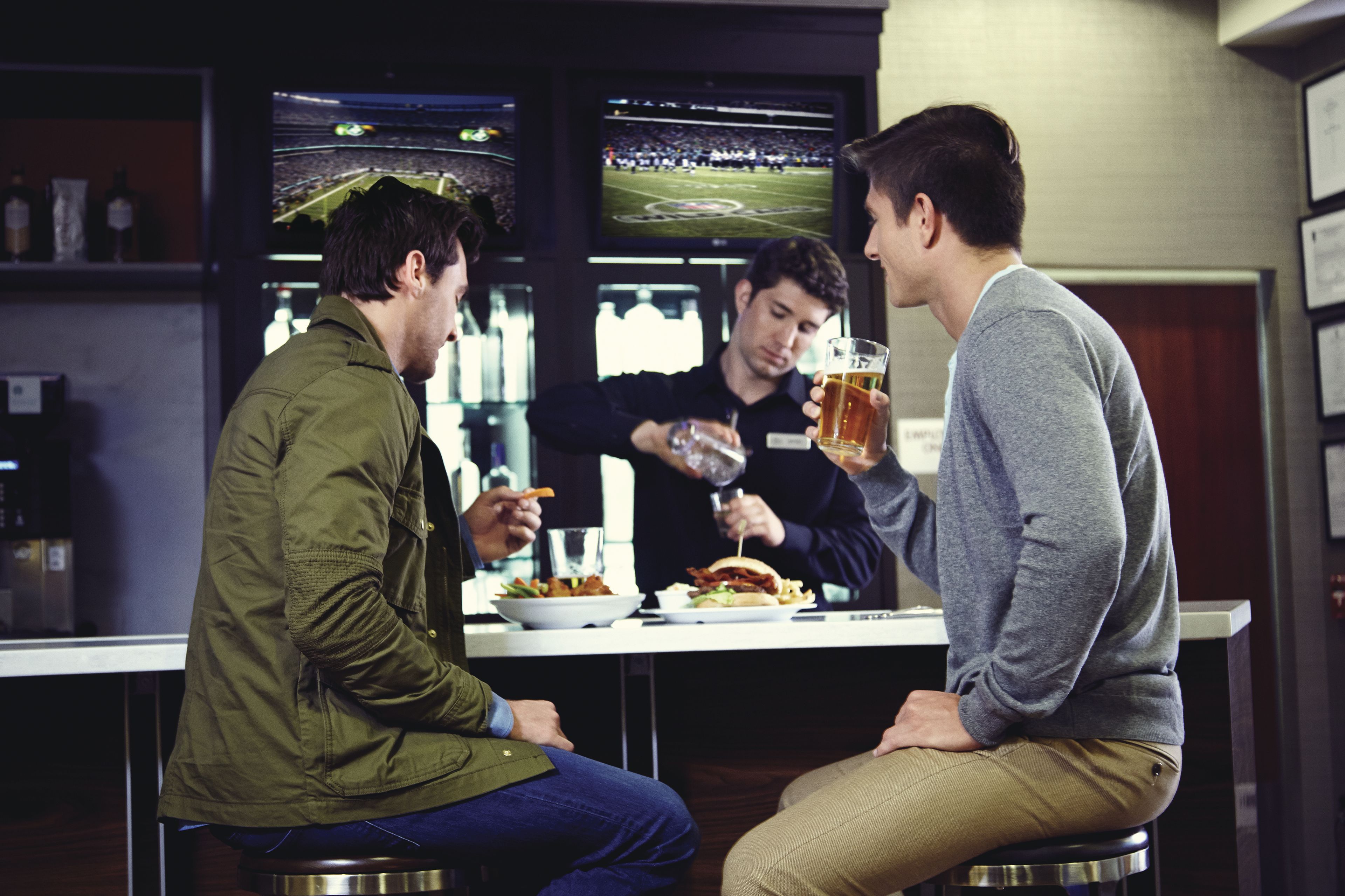 A bar setting with a counter, seating, and multiple screens displaying sports events.