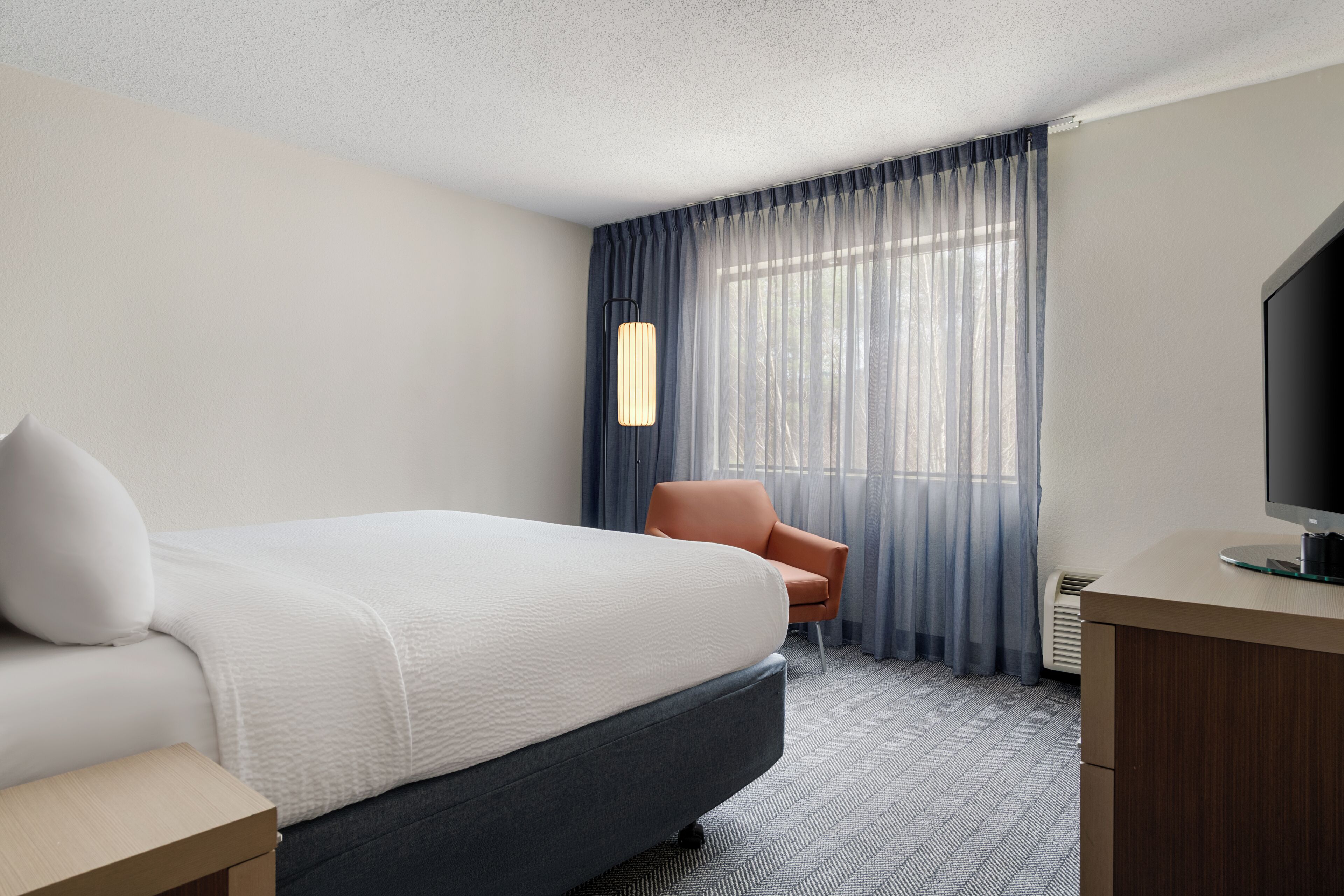A hotel room with a bed, a chair, a desk, a television, and a window with curtains.