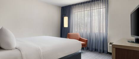 A hotel room with a bed, a chair, a desk, a television, and a window with curtains.