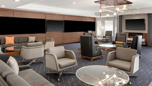 Een moderne hotel lobby met een zithoek, een open haard en een groot televisiescherm.