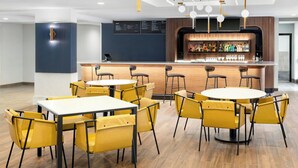Een moderne bar met een houten toonbank, meerdere barkrukken en een menubord.