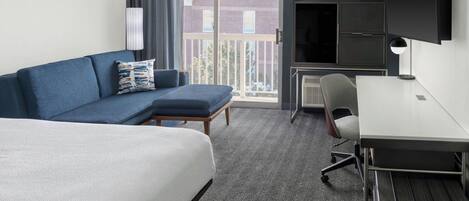 A hotel room with a bed, a sofa, a desk, and a TV.
