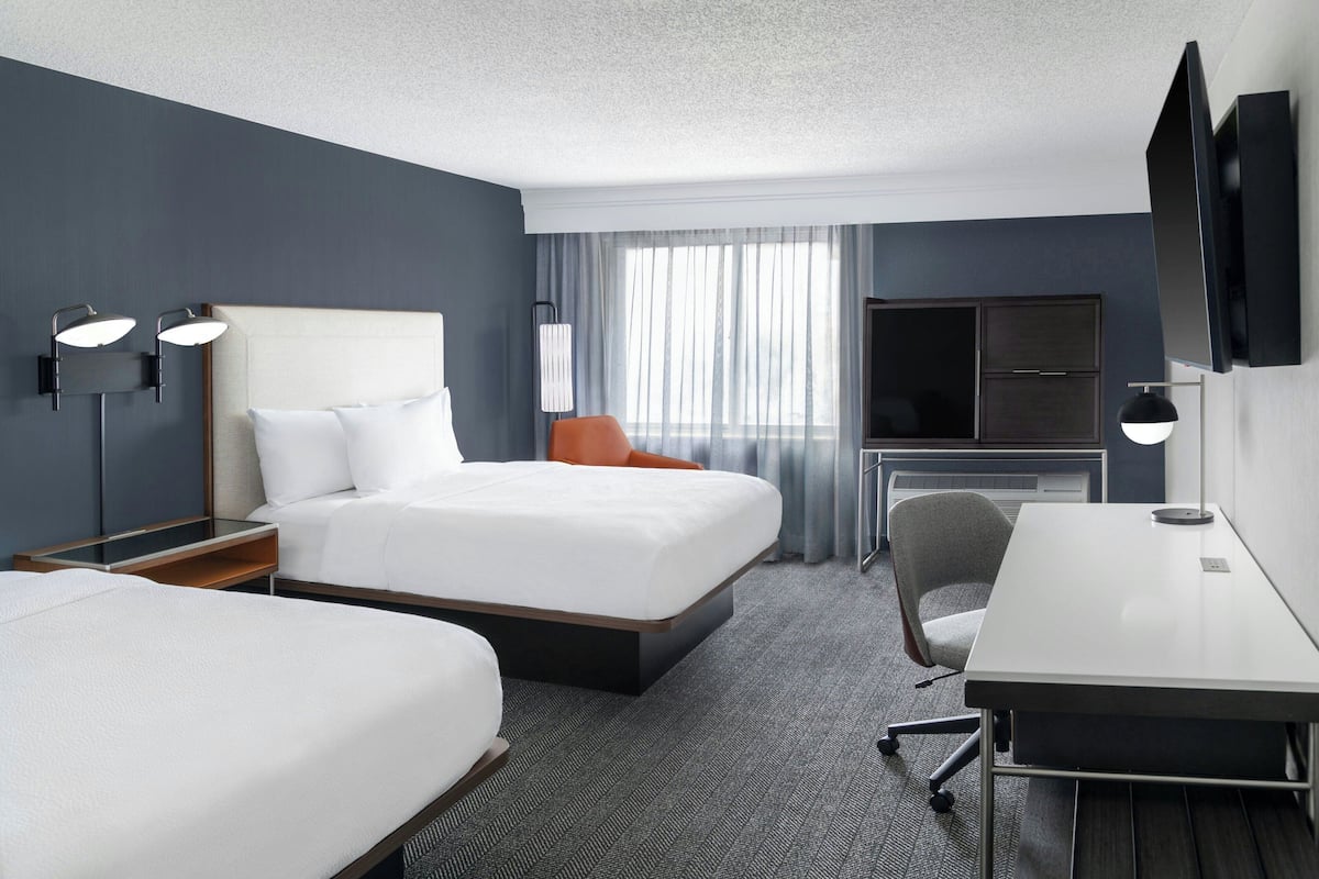 Een hotelkamer met een groot bed, een bureau, een stoel, een televisie en een raam met gordijnen.