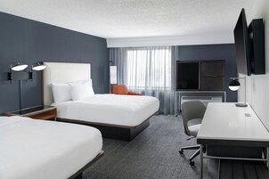 A hotel room with a large bed, a desk, a chair, a TV, and a window with curtains.