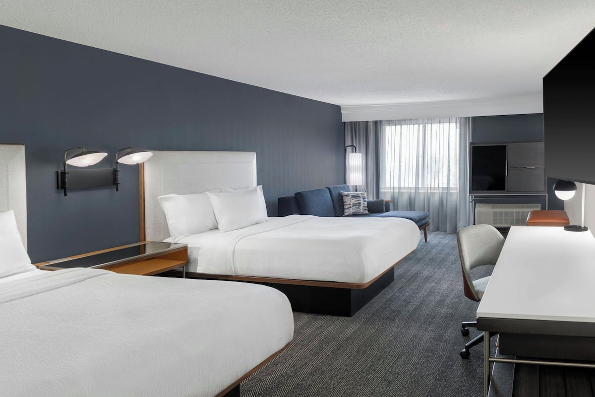 Een hotelkamer met een groot bed, een kleiner bed, een bureau en een televisie.