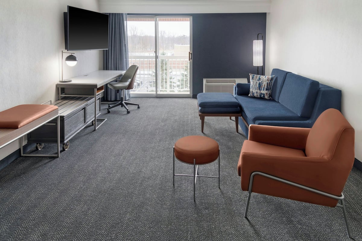 Een hotelkamer met een bureau, stoel, bank, poef en een aan de muur bevestigde televisie.