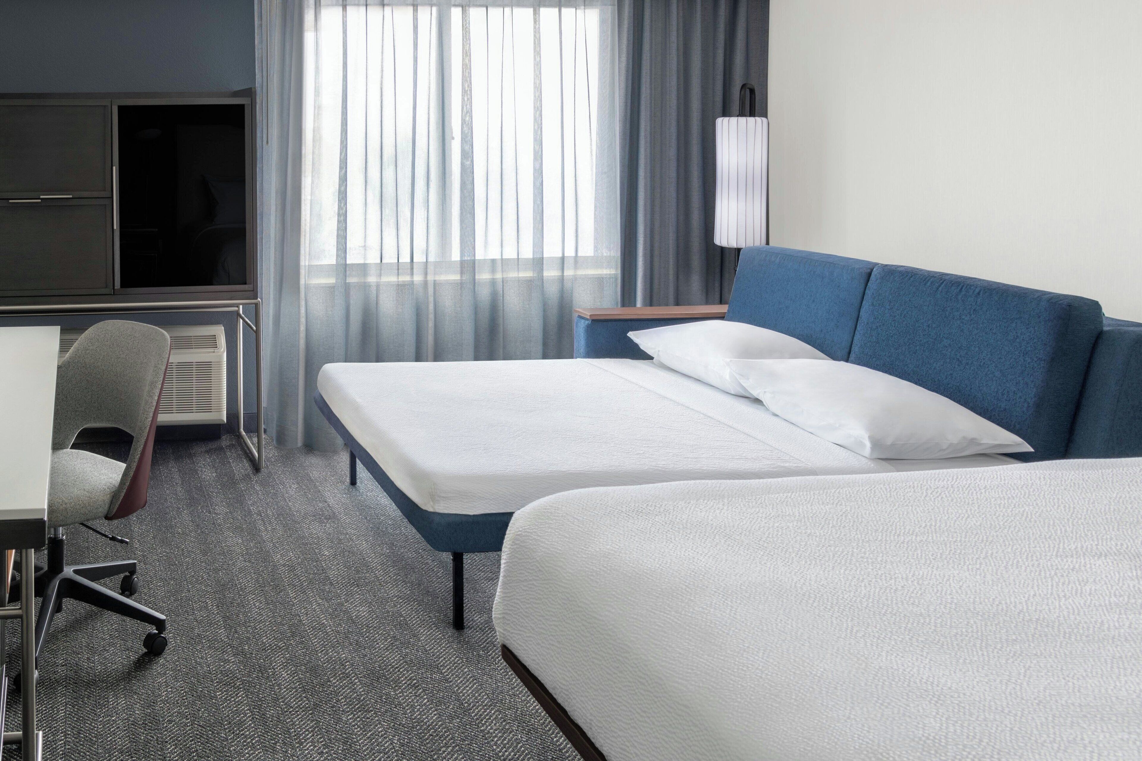 A hotel room with two beds, a desk, a chair, and a TV.
