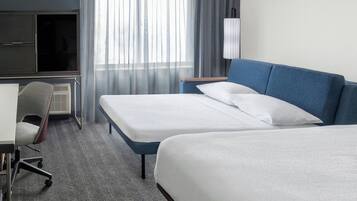 A hotel room with two beds, a desk, a chair, and a TV.