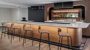 Een barruimte met een lange toonbank, barstoelen, een televisie boven de bar en een plank met verschillende flessen en glazen.