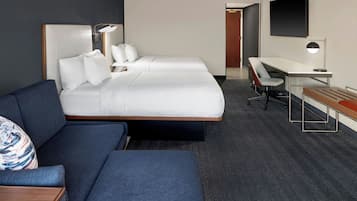 A modern hotel room with a large bed, a desk, a chair, and a sofa.
