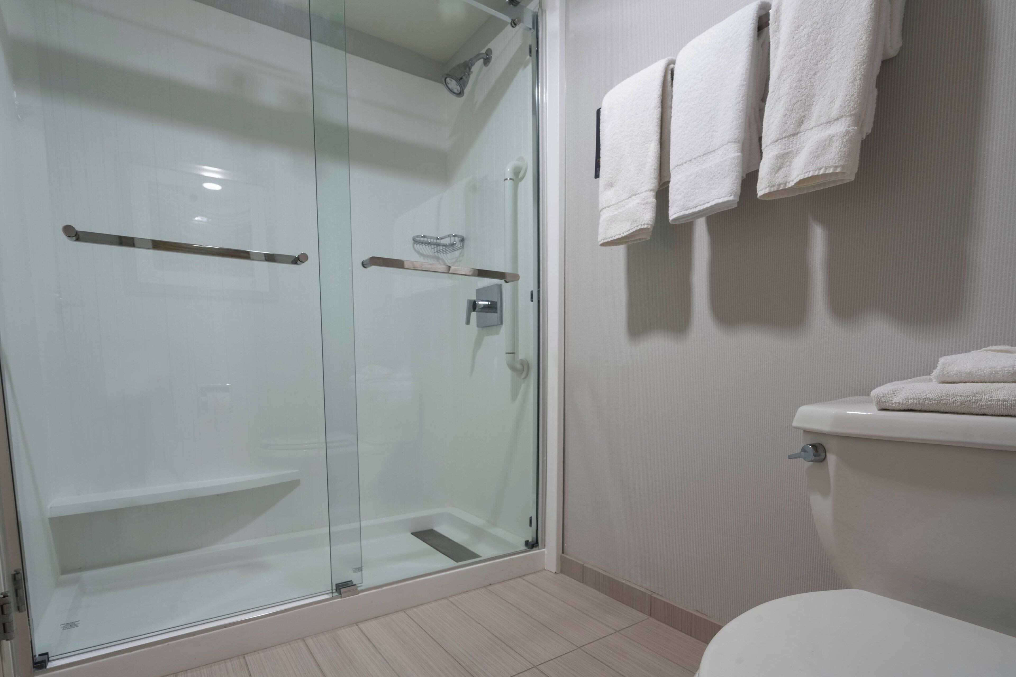 A modern bathroom with a glass-enclosed shower, a toilet with a towel rack, and a shelf with a glass container.
