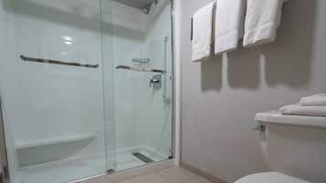A modern bathroom with a glass-enclosed shower, a toilet with a towel rack, and a shelf with a glass container.