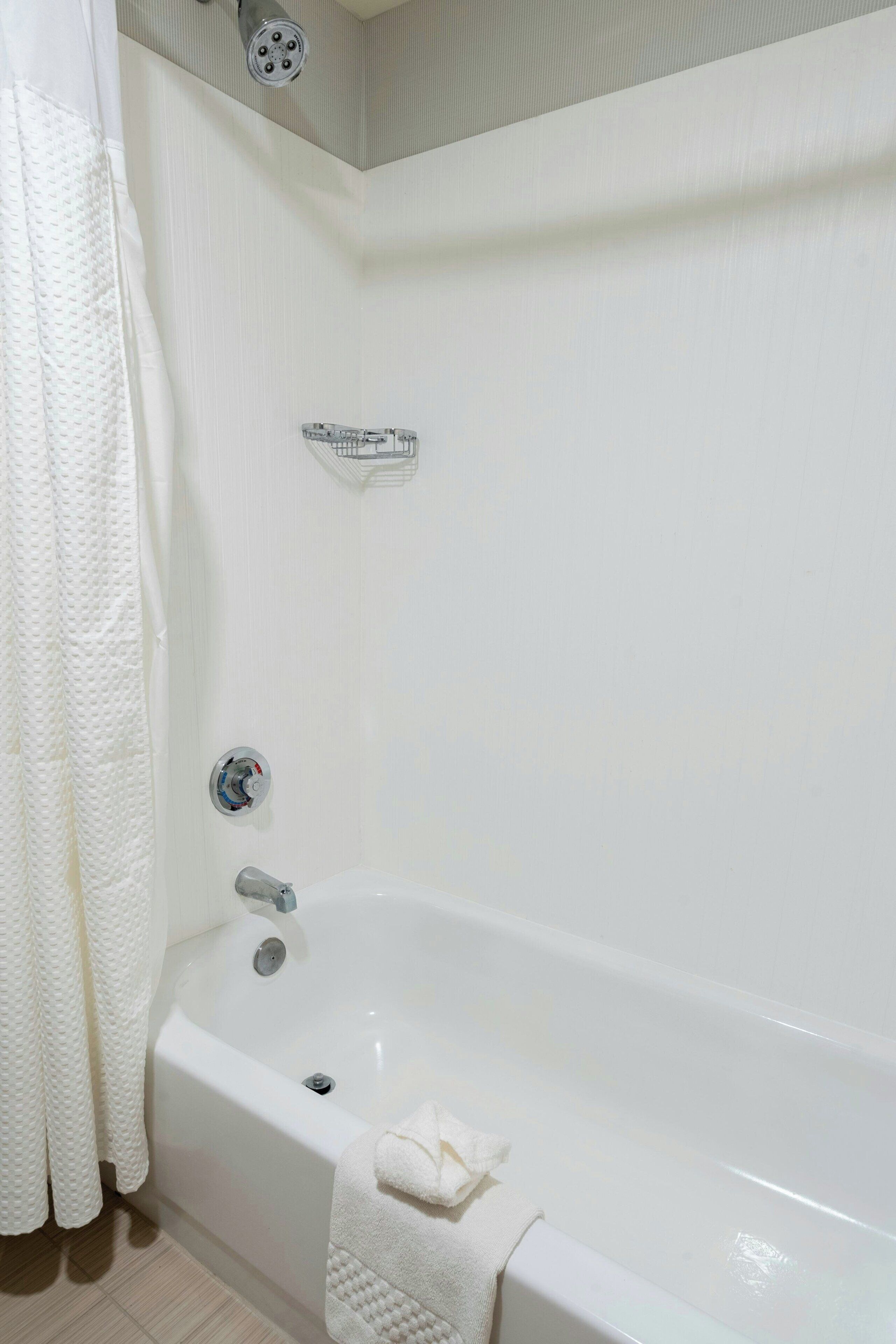 Une salle de bain avec une baignoire blanche, une pomme de douche, un porte-serviettes et un étagère pour la douche.