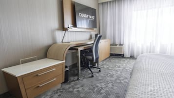 A hotel room with a desk, chair, and bed.