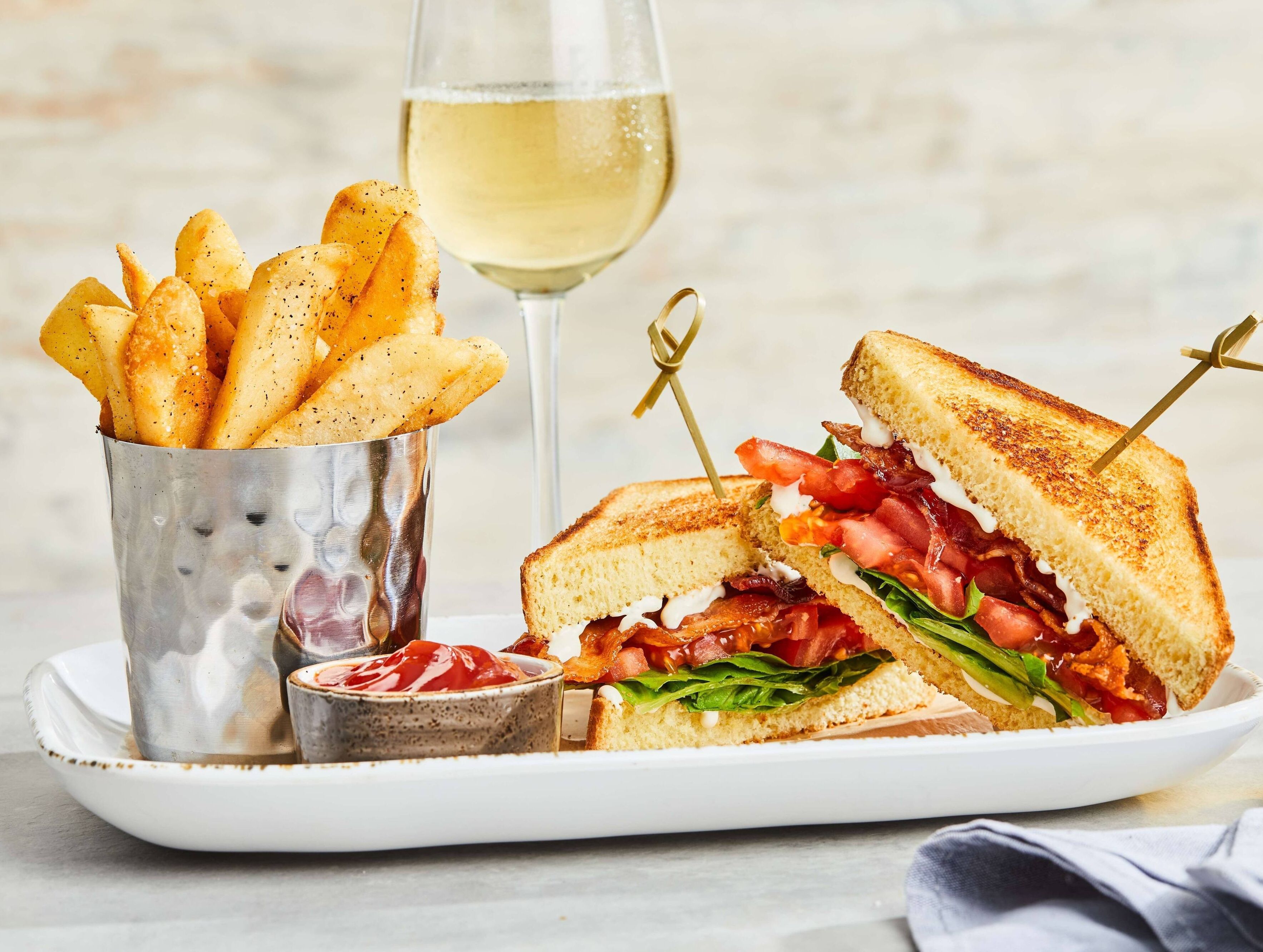 A sandwich with a side of fries and a glass of white wine on a plate.
