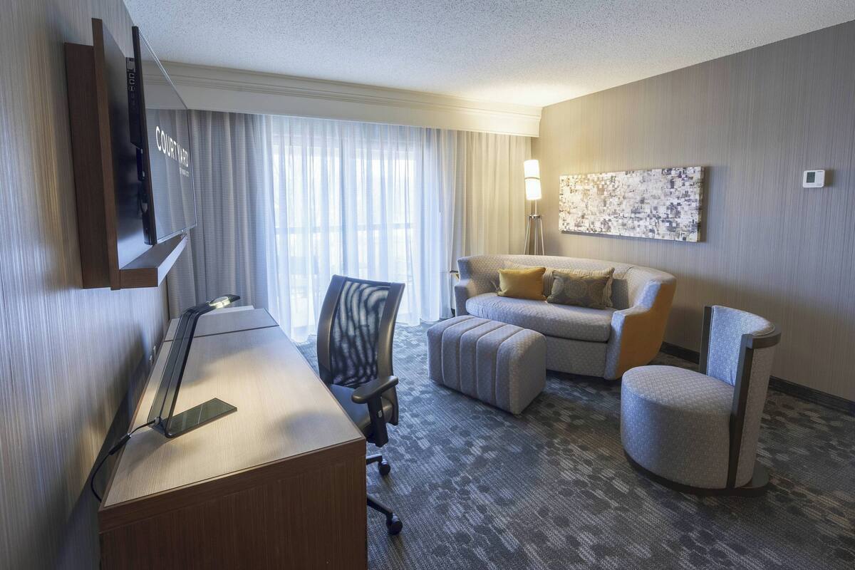A hotel room with a desk, a chair, a sofa, and a small armchair.