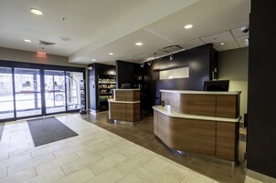 Zona de recepción con mostrador, puerta de cristal grande y un pequeño quiosco al fondo.
