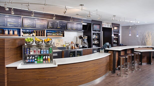 Un área de bar moderna con una barra curva, varios dispensadores de bebidas y una selección de botellas y vasos.