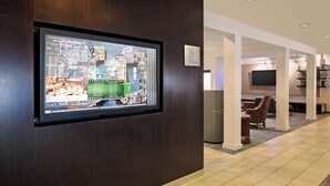Un vestíbulo de hotel con un panel informativo digital, una zona de estar y un televisor montado en la pared.