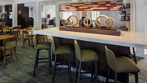 Un área de bar moderna con un mostrador de madera, taburetes tapizados en verde y una lámpara decorativa colgante.