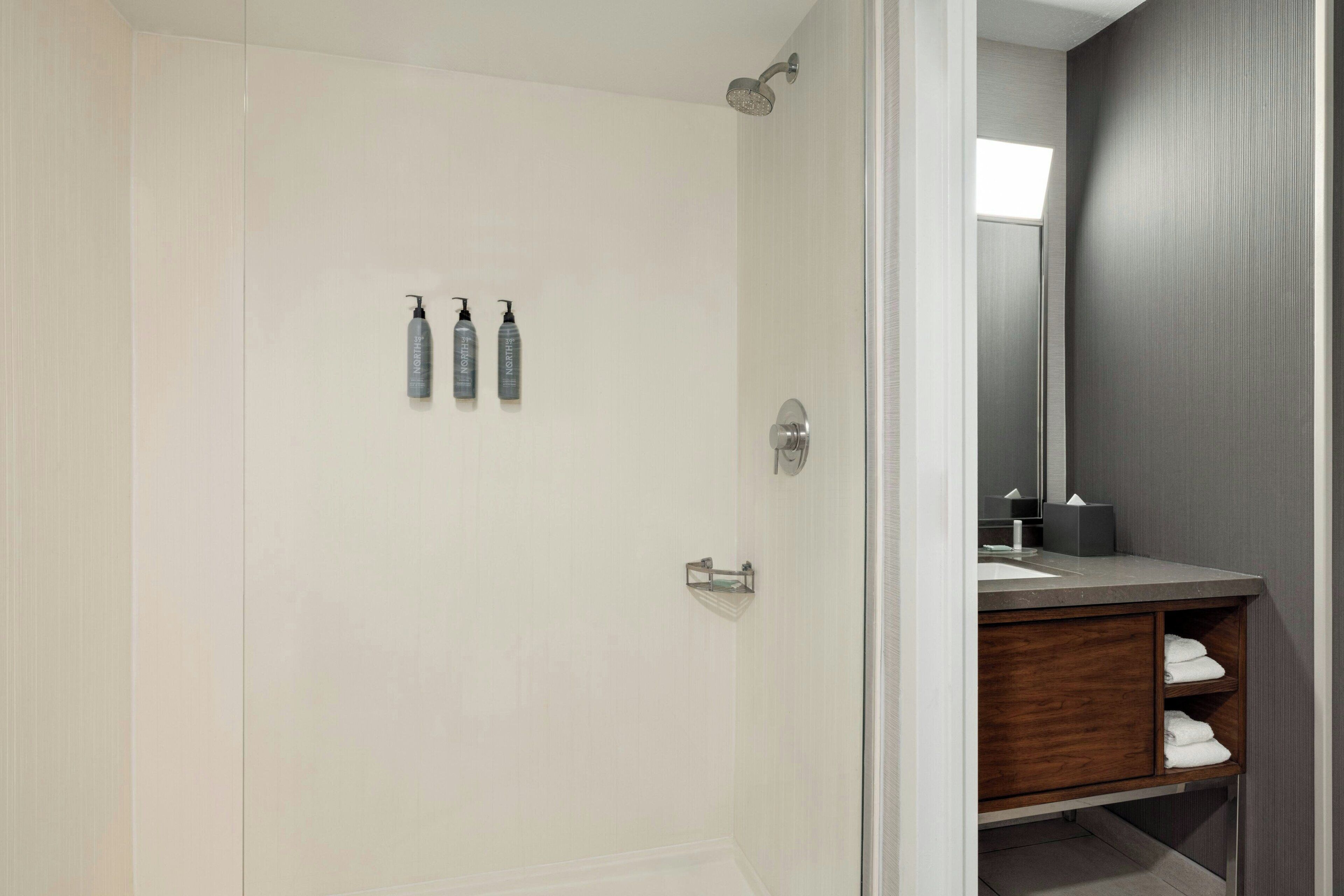 A modern bathroom with a shower, a vanity with a mirror, and three bottles of shampoo on the wall.
