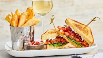 Un plato con un sándwich a la plancha, una copa de vino blanco y un recipiente con papas fritas.