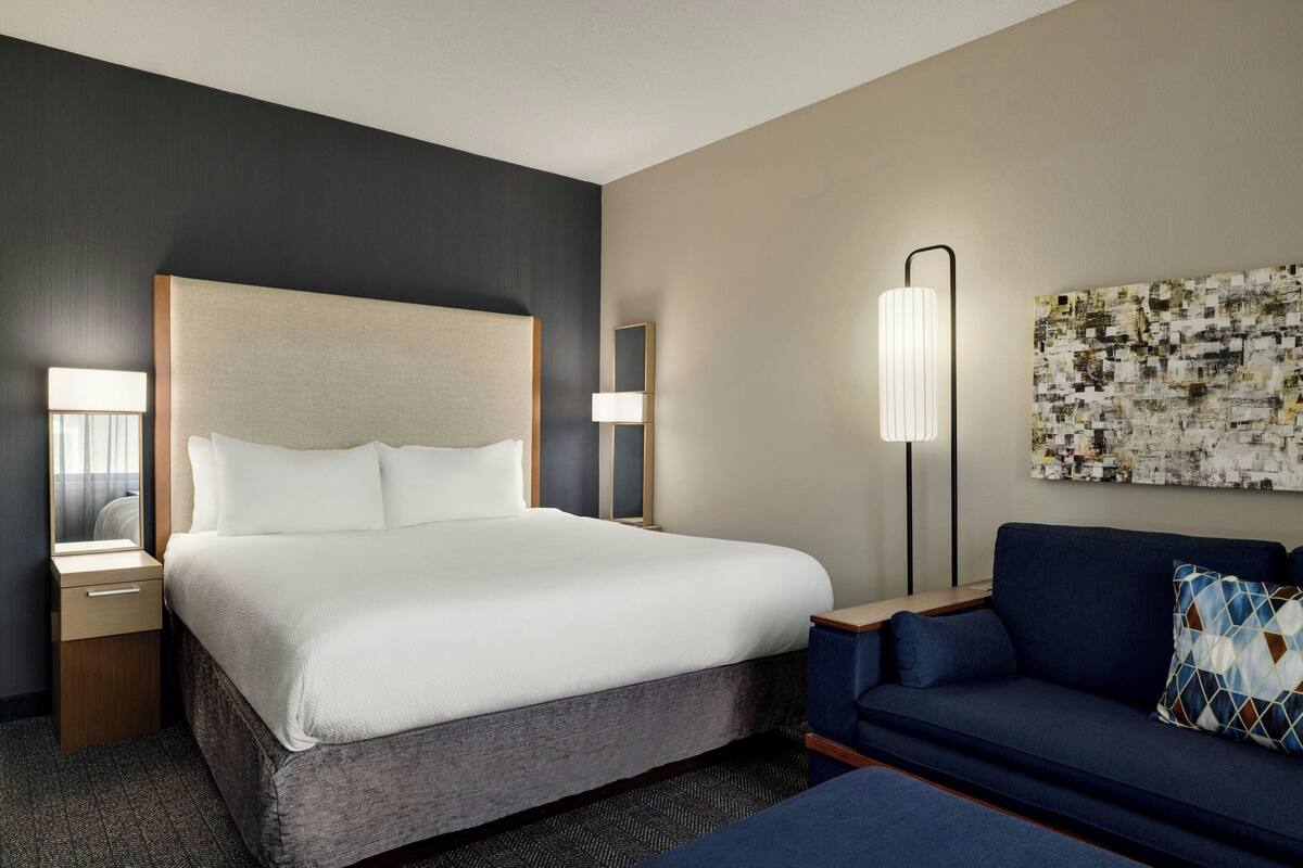 Ein Hotelzimmer mit einem großen Bett, einer Couch, einem Nachttisch, einer Lampe und einem Wandbild.