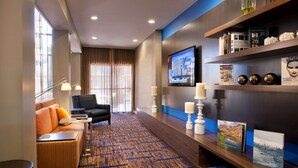 Una hall d'albergo con divano, poltrone, televisore, libreria e tappeto decorato.