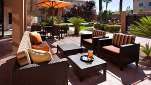 Area patio esterna con mobili in vimini, tra cui divani e tavoli, e un ombrellone grande che offre ombra.