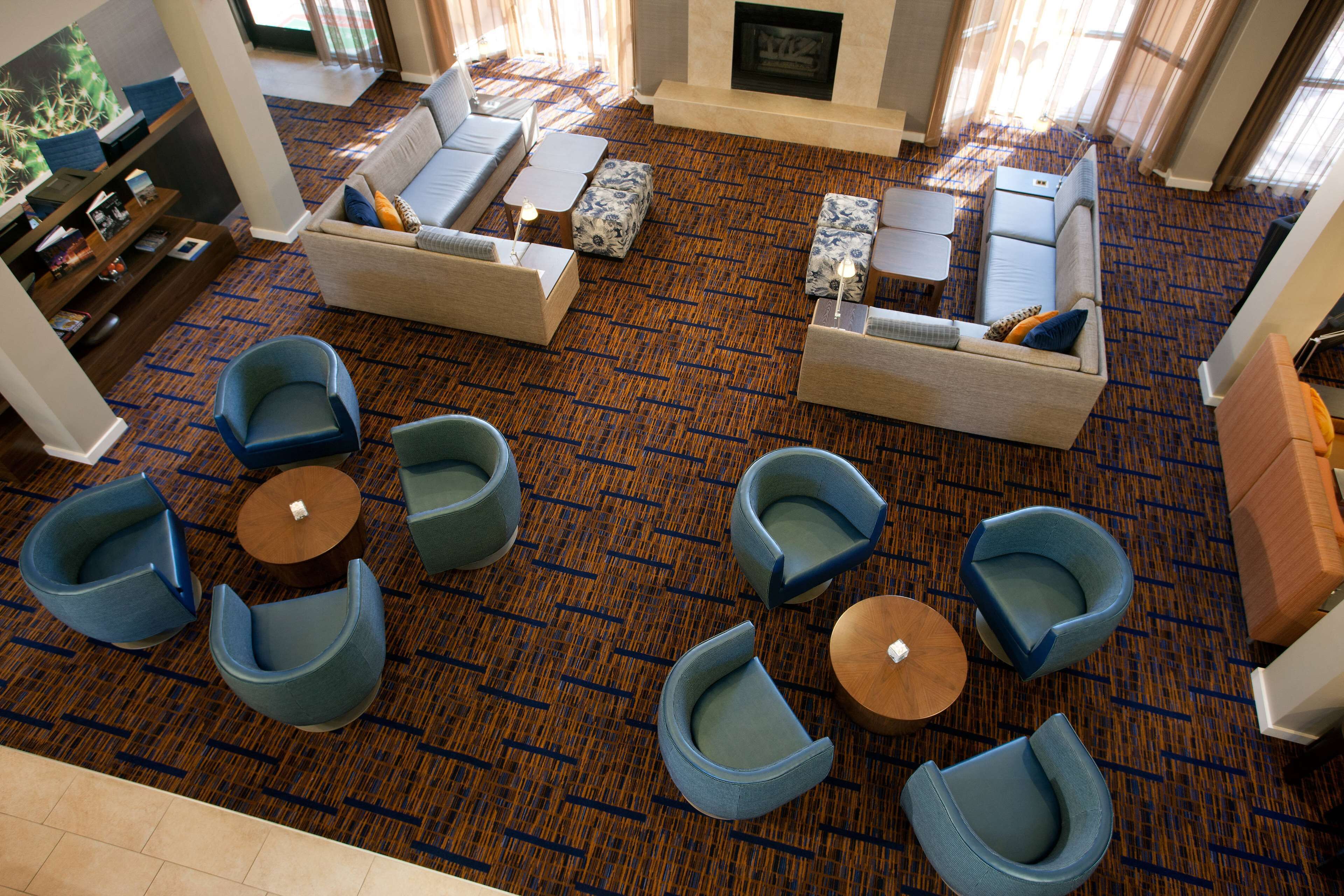 Un hall de hotel con alfombra estampada, sofás, sillones y un televisor.
