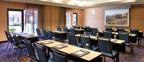 A conference room with multiple tables and chairs, a projector screen, and a carpeted floor.