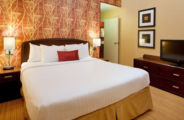 A neatly made bed with white and red bedding, a television on a wooden stand, and two framed pictures on the wall.