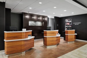 A reception area with three wooden reception desks, a black wall with a 'Courtyard Marriott' sign, and a modern light fixture.