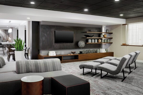 A modern living room with a large flat-screen TV mounted on the wall, a grey sofa, a coffee table, and a patterned rug. - Courtyard by Marriott Milwaukee Downtown (Milwaukee)