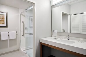 A modern bathroom with a glass shower enclosure, a white sink with a wooden vanity, and a large mirror. - Courtyard by Marriott Milwaukee Downtown (Milwaukee)