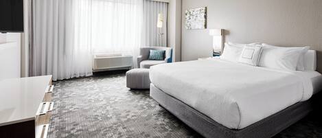 A hotel room with a large bed, a desk, a chair, and a window with curtains.