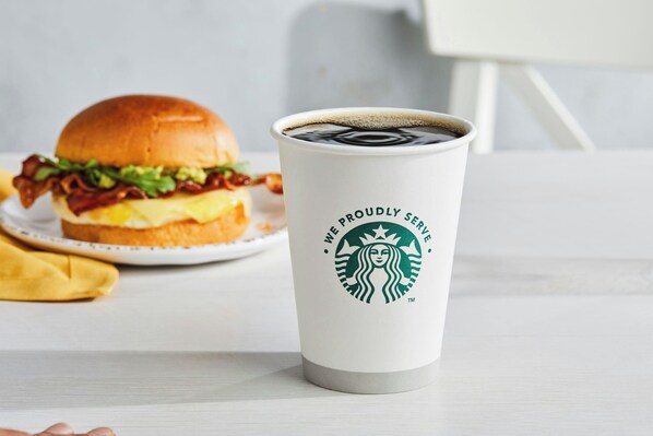 A white cup with a Starbucks logo and text, a burger, and a yellow napkin on a white table. - Courtyard by Marriott Milwaukee Downtown (Milwaukee)
